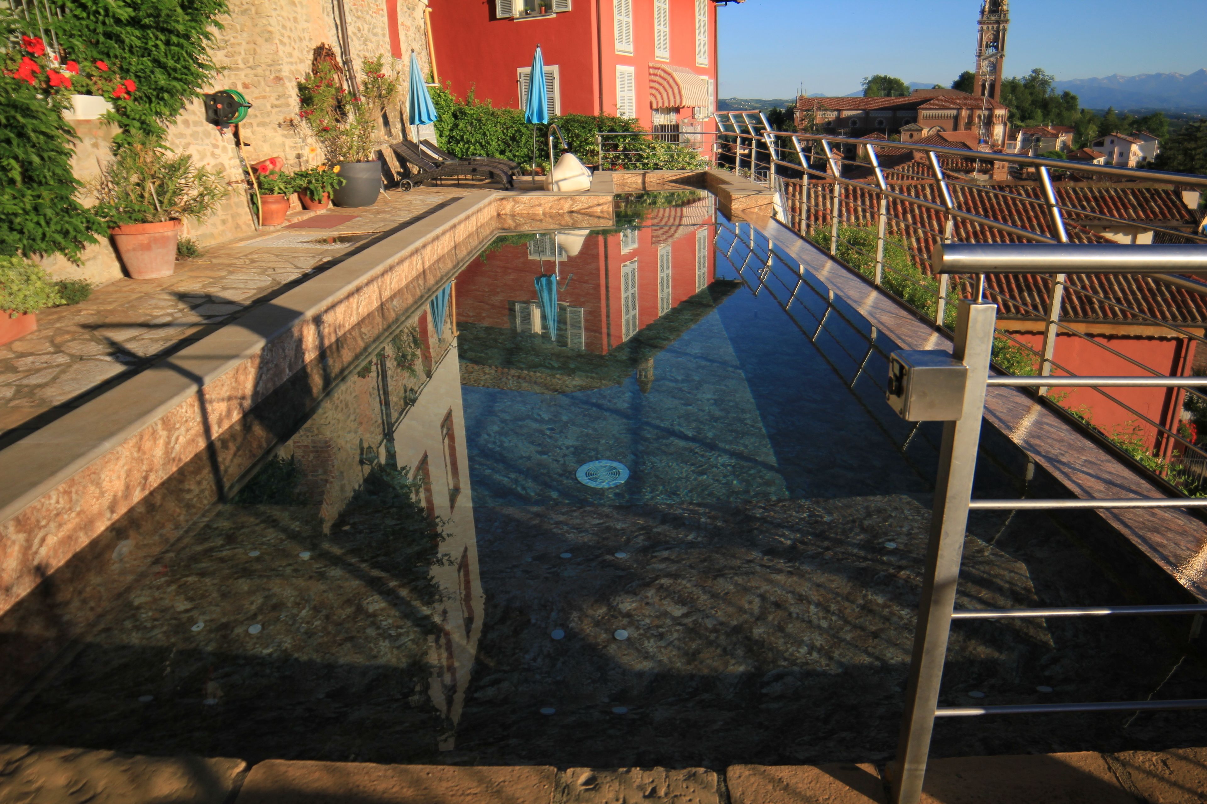 Una piscina con superficie de agua cristalina, rodeada de muros de piedra y plantas en macetas.