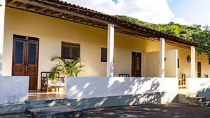 Edifici amb un porxo cobert, una porta de fusta i una petita zona de jardí amb una palmera.