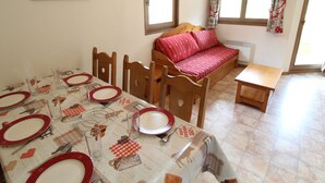 A dining area with a table set for four, a wooden sofa, and a small wooden table.
