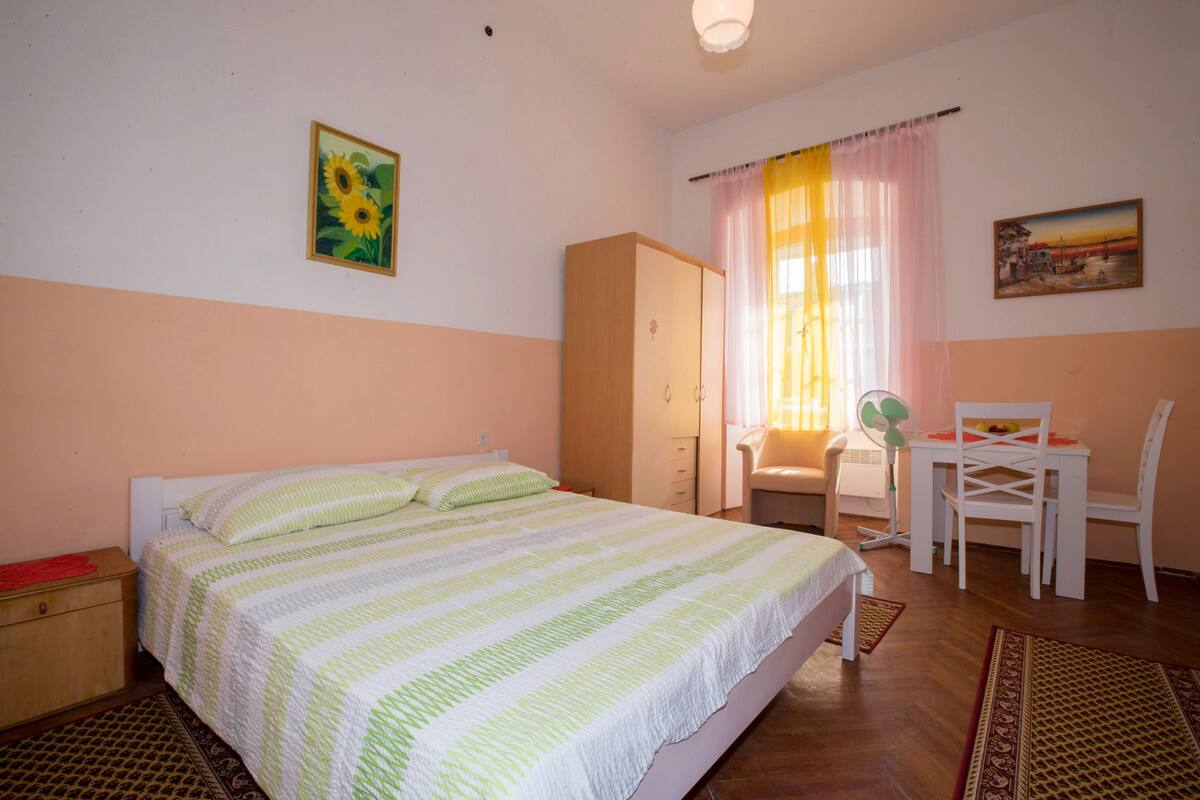 Une chambre à coucher comprenant un lit, une armoire, un bureau avec des chaises et une fenêtre avec des rideaux.