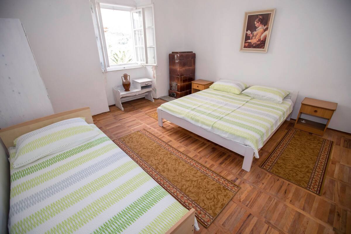 Une chambre avec deux lits, un plancher en bois, une fenêtre, un bureau et un tableau accroché au mur.