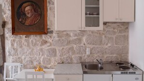 Una cocina con pared de piedra, armarios blancos, un cuadro enmarcado y un pequeño comedor con mesa y sillas blancas.