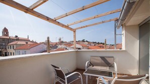 Un balcón con dos sillas y una mesa, con vista a un pueblo de edificios con tejados rojos.