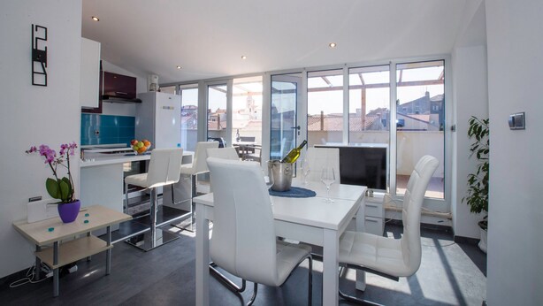 Una cocina moderna con armarios blancos, una encimera azul y un comedor con sillas y mesa blancos.