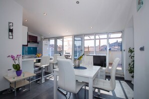 Eine moderne Küche mit weißen Schränken, einer blauen Arbeitsplatte und einem Essbereich mit weißen Stühlen und einem Tisch.