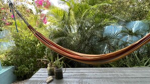 A hammock on a wooden deck surrounded by lush greenery and flowering plants.