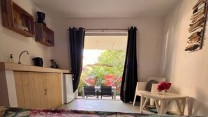 A bedroom with a bed, a small kitchenette, a dining area with a table and chairs, and a view of the outdoors.