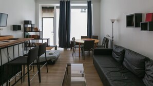 A modern living room with a black leather sofa, a wooden dining table with chairs, a glass coffee table, and a TV on the left. - Souplex - 4P - Paris city center (Paris)