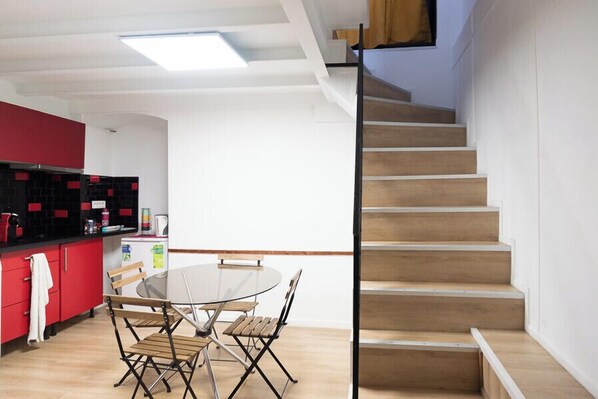 Una cocina moderna con armarios rojos, una mesa redonda para comer y una escalera de madera.