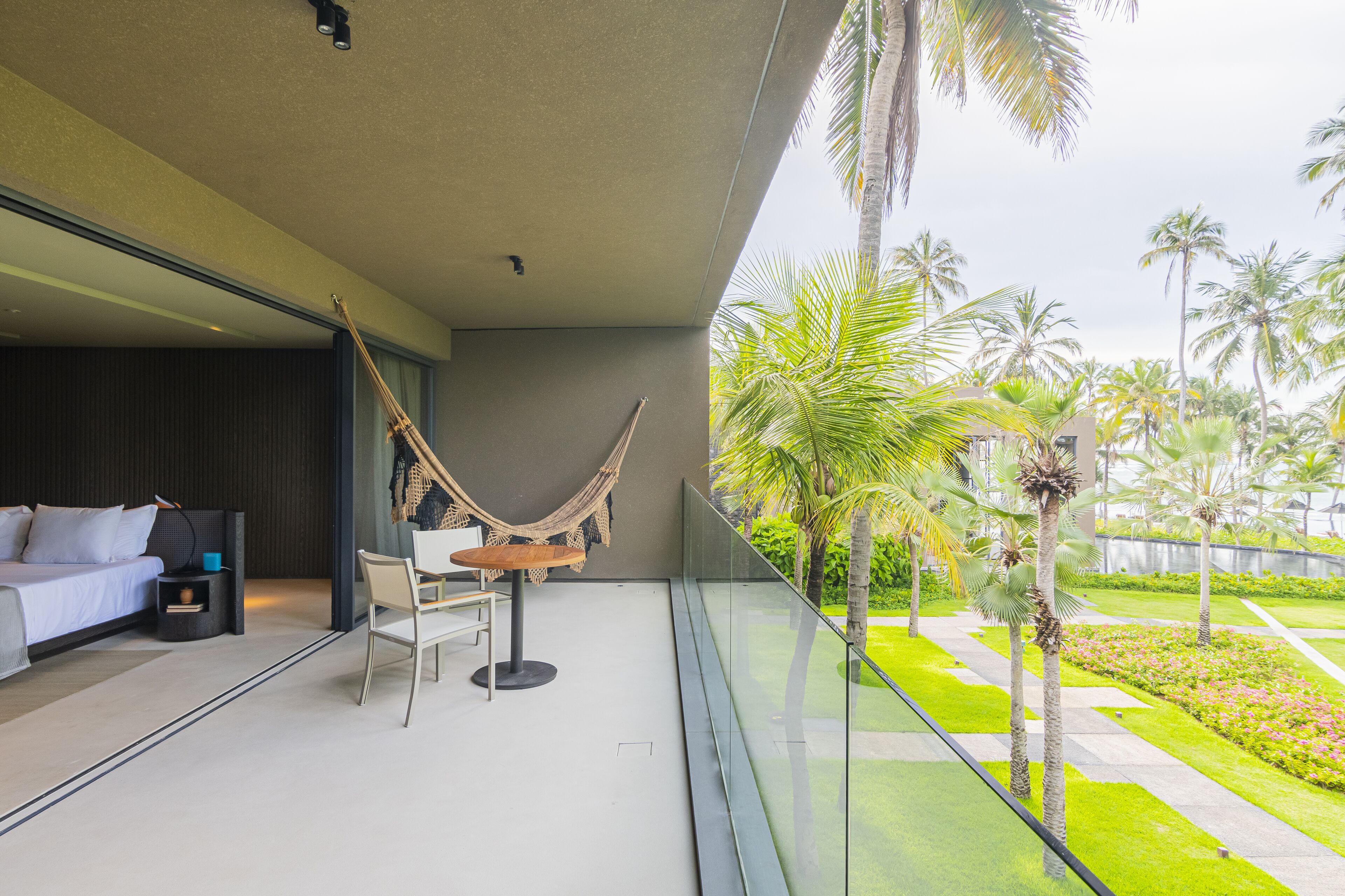Una habitación de hotel moderna con un balcón, una hamaca, una cama, una mesita y una silla.