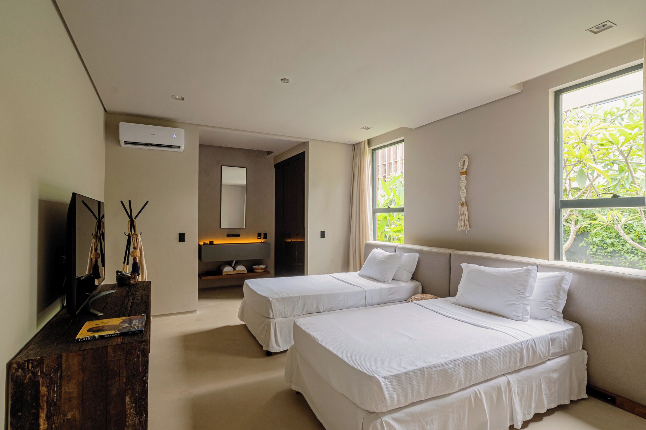 Une chambre d’hôtel moderne, équipée de deux lits, d’une télévision, d’un bureau en bois et d’une grande fenêtre donnant sur un paysage verdoyant.