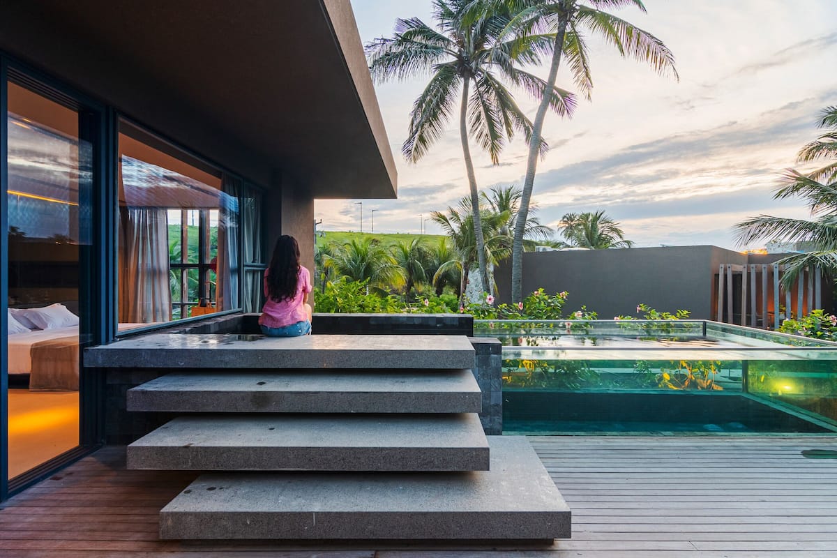 Un espace extérieur moderne avec une piscine, des palmiers et une personne assise sur des marches.