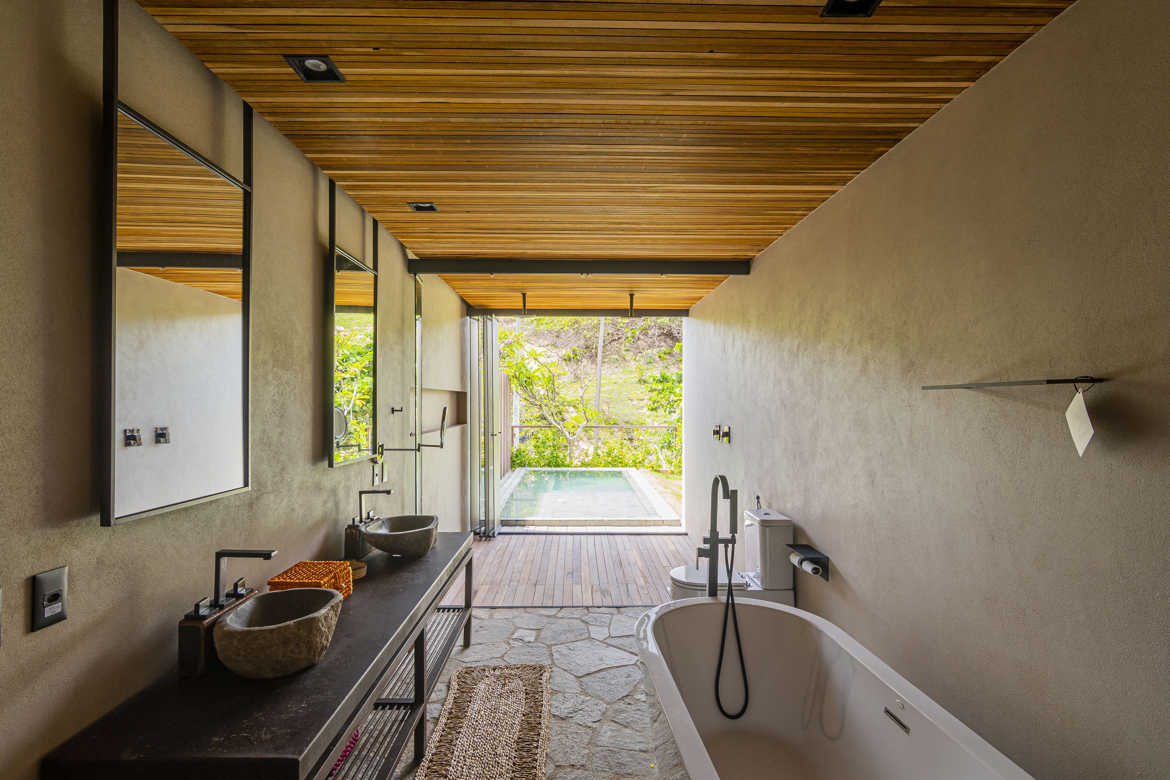 A modern bathroom with a large bathtub, a stone sink, and a wooden ceiling.