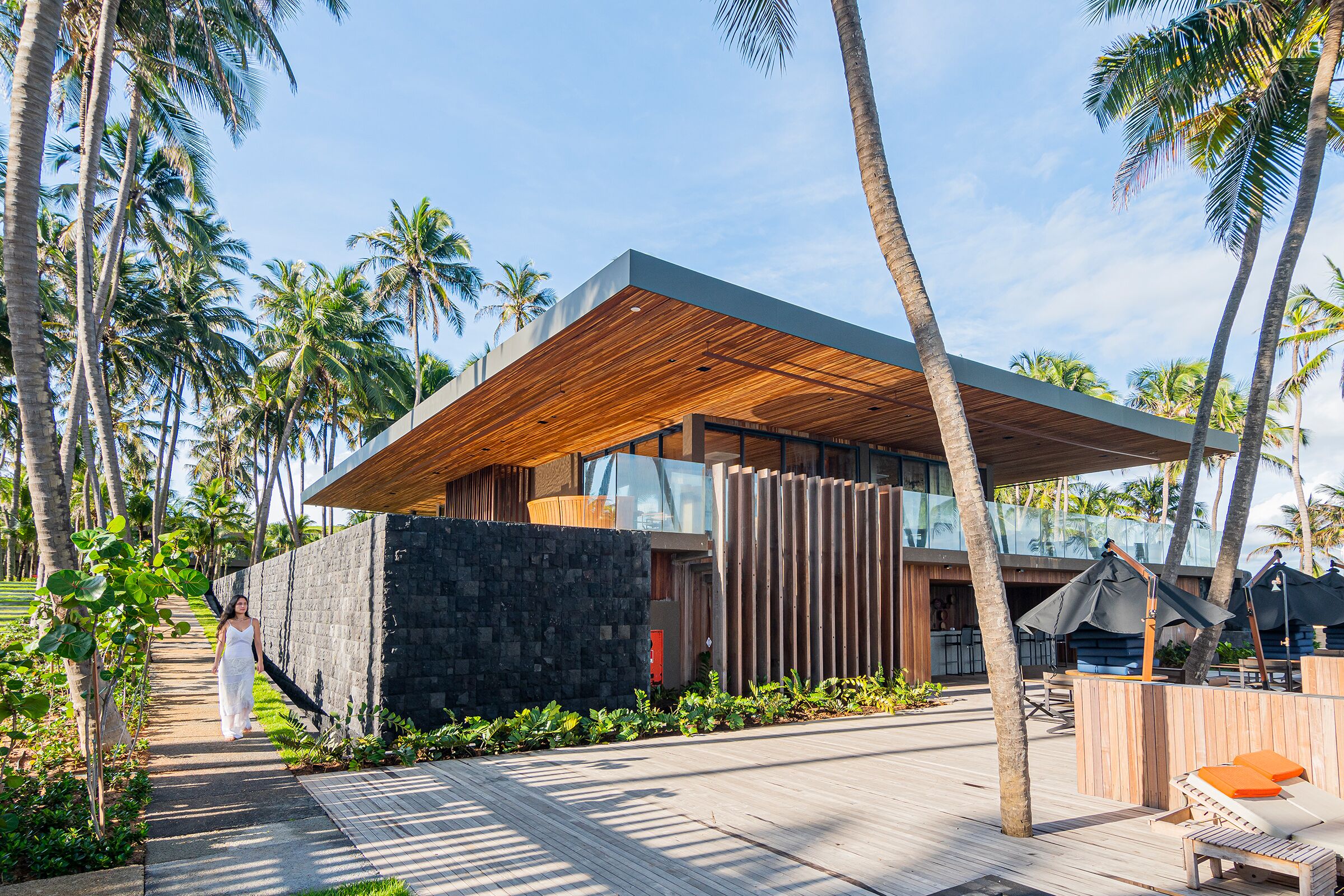 A modern building with a wooden deck, surrounded by palm trees and a clear sky.