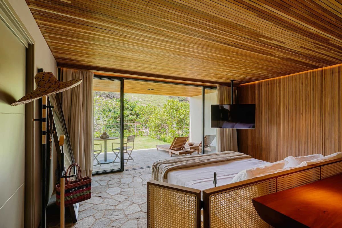 Une chambre moderne avec un grand lit, un téléviseur fixé au mur et une vue sur le jardin extérieur.