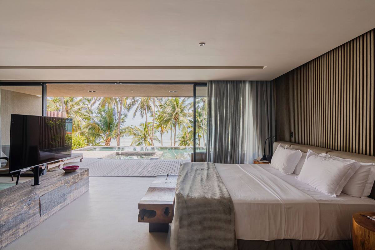 Une chambre d’hôtel moderne avec un grand lit, une télévision et une vue sur une piscine et des palmiers.
