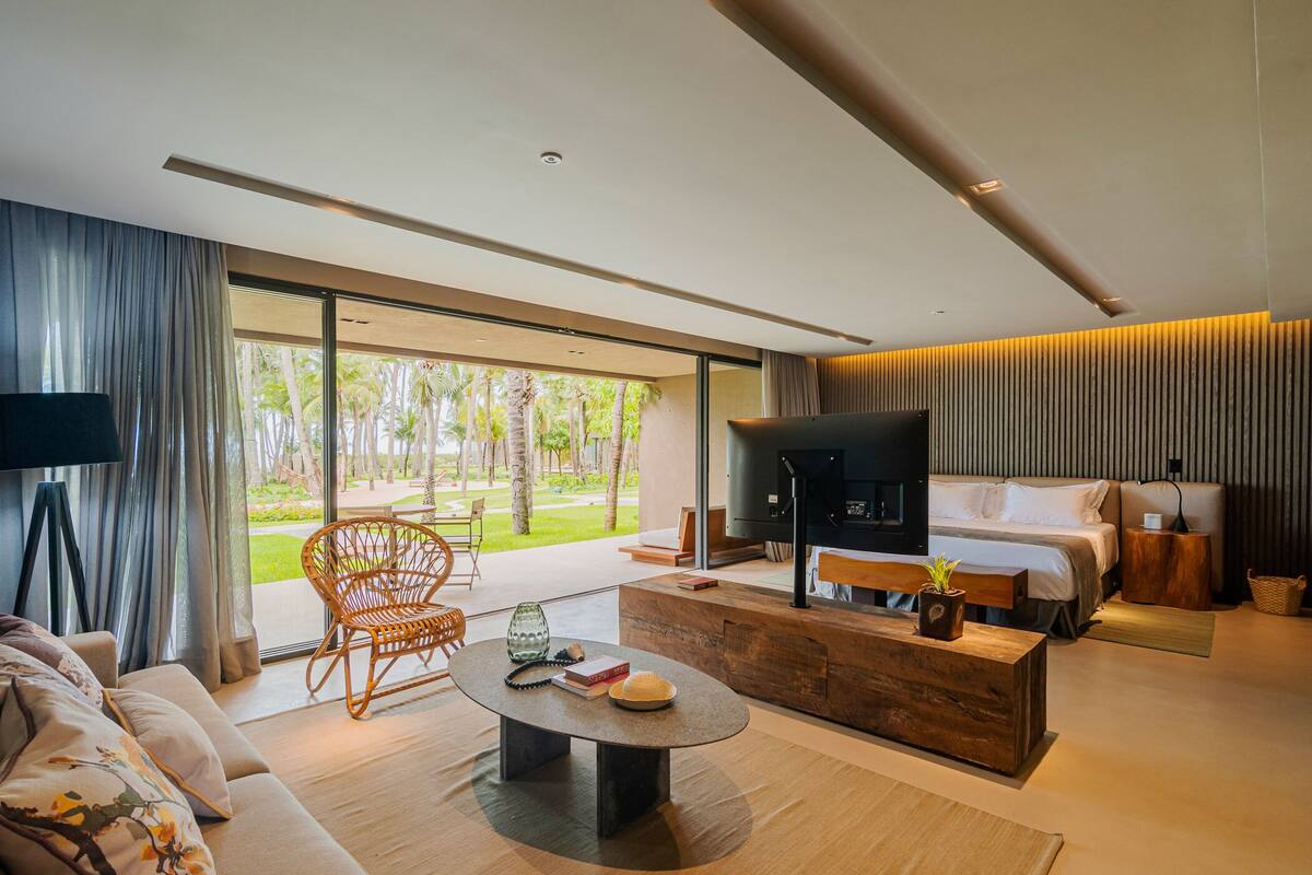 Une chambre d’hôtel moderne avec un grand lit, une télévision, une table basse en bois et une vue sur le jardin.