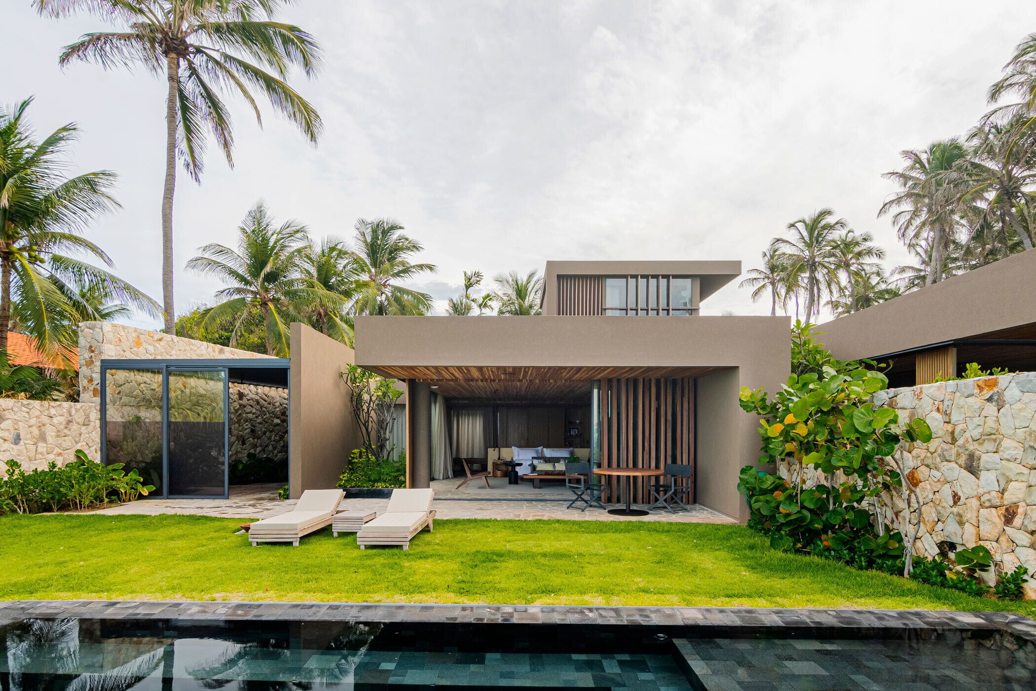 A modern house with a swimming pool, a covered patio, and a stone wall.