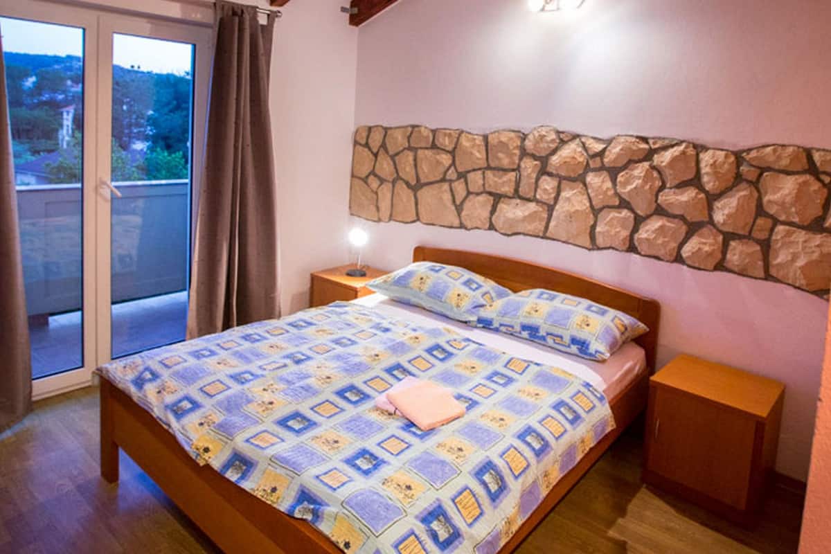 Un dormitorio con techo de madera, pared de piedra, cama con colcha estampada, mesita de noche y puerta corredera de vidrio que da a un espacio exterior.