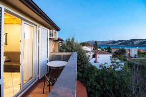 Un balcón con mesa y sillas, con vista a una zona costera con casas y colinas.