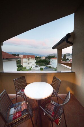 Un balcón con una mesa redonda y cuatro sillas, con vista a una zona residencial con edificios y una montaña al fondo.