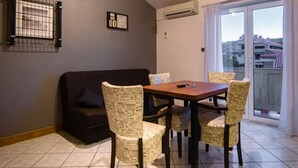 A dining area with a wooden table and chairs, a dark sofa, and a view through a glass door to the outside. - Apartment Sanic Rab (Lopar)