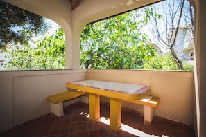A patio with a yellow table and benches, surrounded by a white wall and a window overlooking greenery. - Apartment Sanic Rab (Lopar)