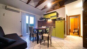 A compact kitchen with a dining area, a sofa, and a view through a glass door. - Apartment Sanic Rab (Lopar)