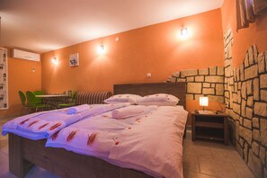Habitación de hotel con cama, una mesita con lámpara, una silla y pared de piedra.
