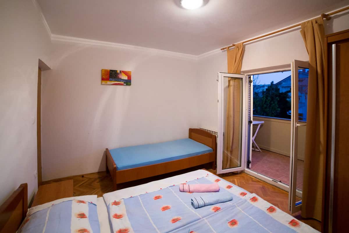 Un dormitorio con una cama individual, una mesita pequeña y un ventanal corredizo que da a un balcón.