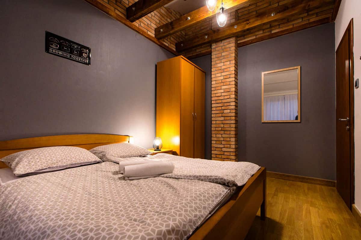 Un dormitorio con una cama de madera, un pilar de ladrillo, un armario y un espejo en la pared.