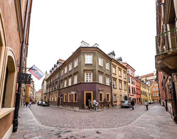 En kullerstensgata med historiska byggnader, en flagga och människor som promenerar.