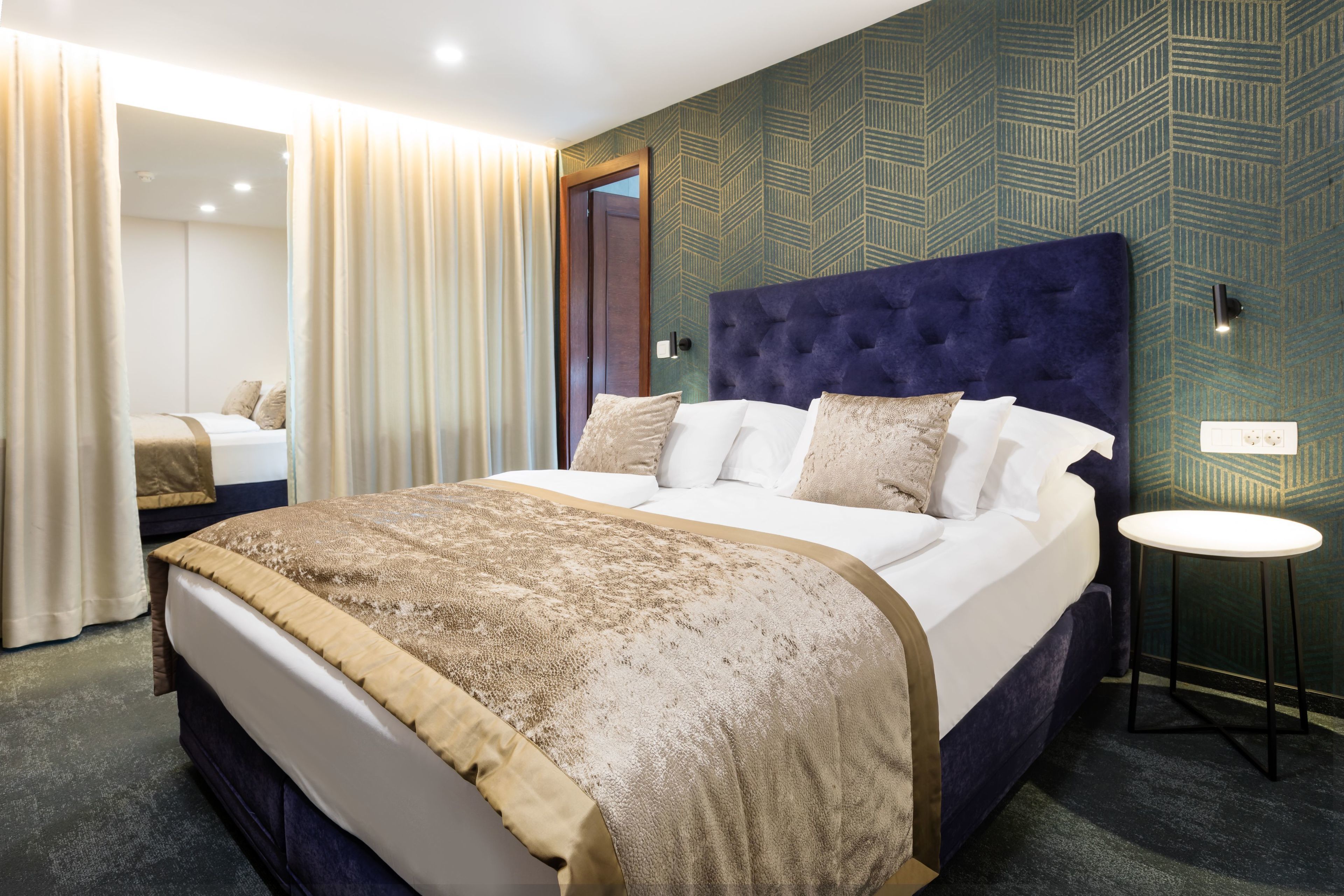 Una habitación de hotel con una cama grande, una mesita de noche y un papel tapiz estampado.