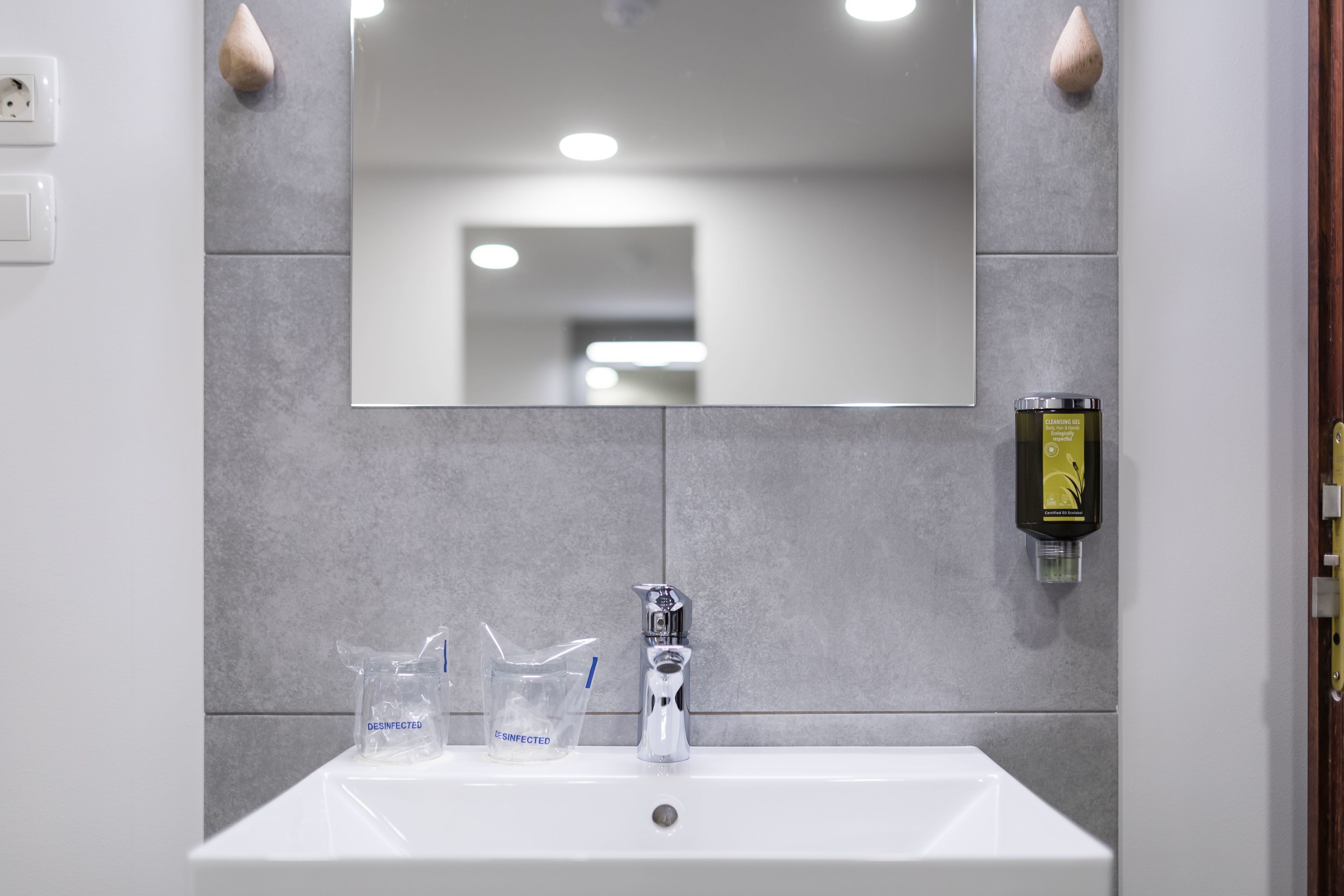 A bathroom with a white sink, a mirror, and a hand sanitizer dispenser.