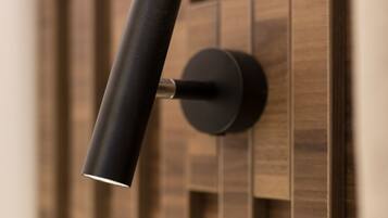 A modern wall-mounted light fixture with a cylindrical shade and a round base, set against a wooden panel background.