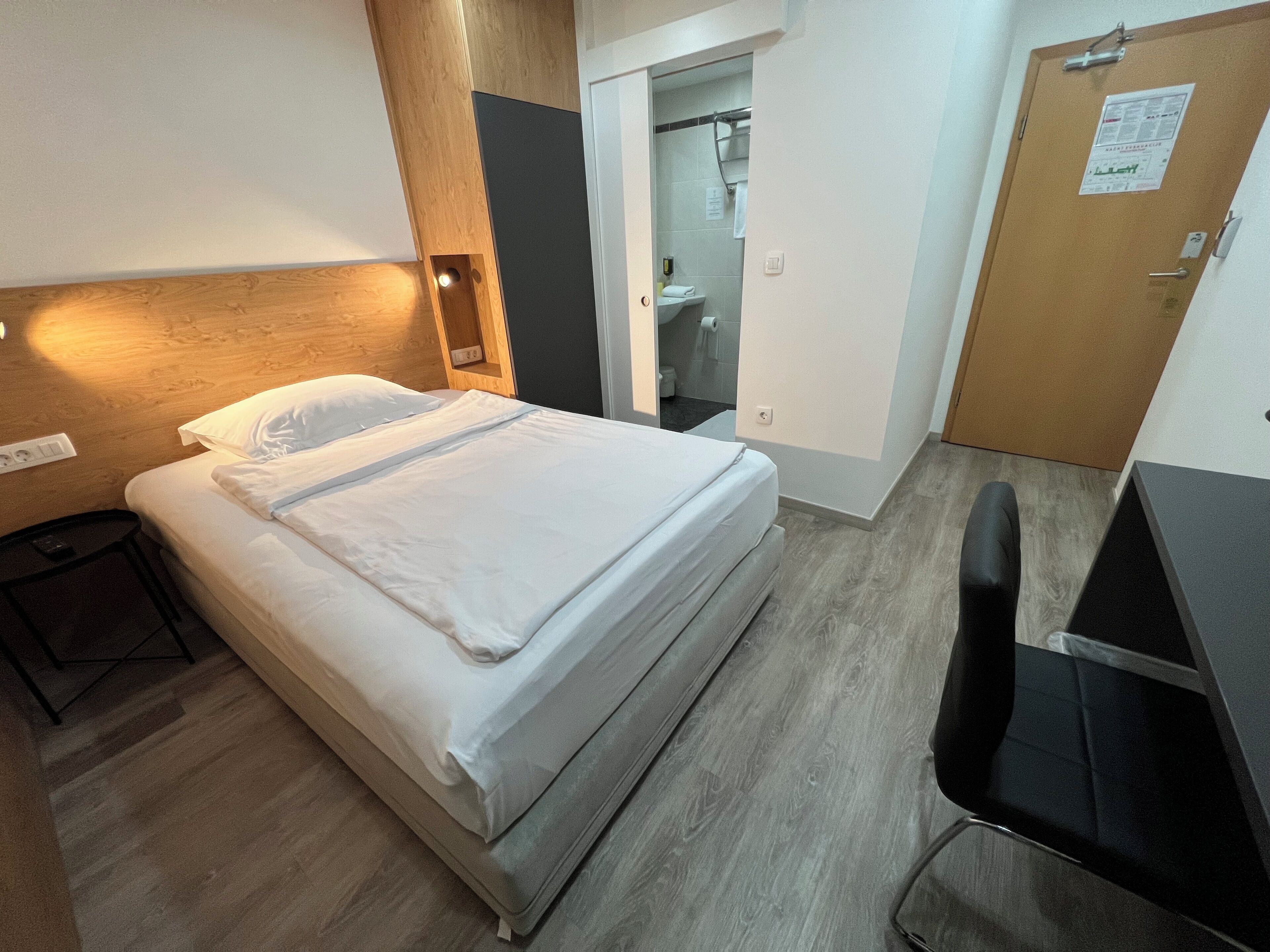 A hotel room with a bed, a desk, and a bathroom visible through an open door.