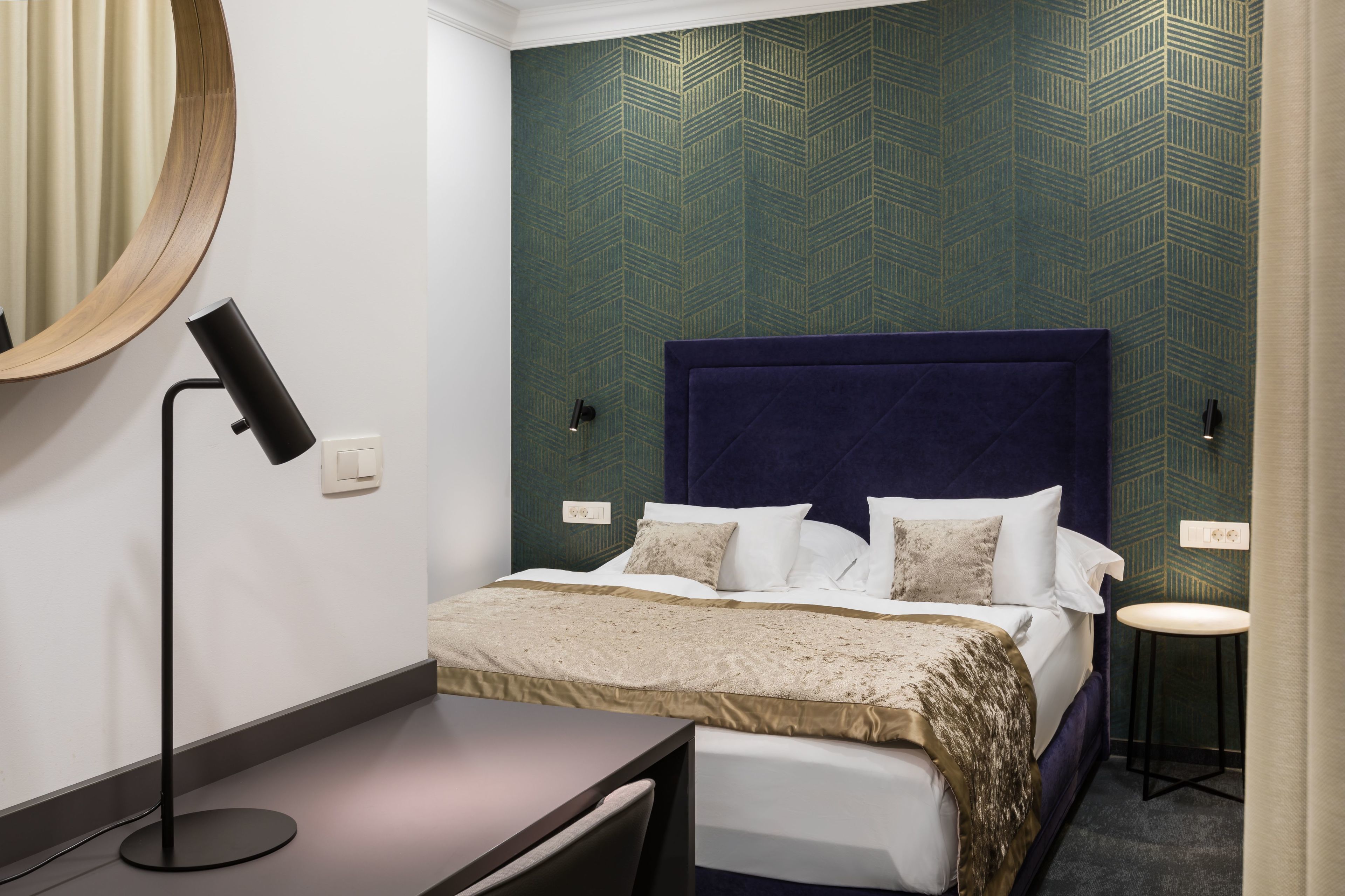 A neatly arranged hotel room with a large bed, bedside tables, a desk, and a mirror.