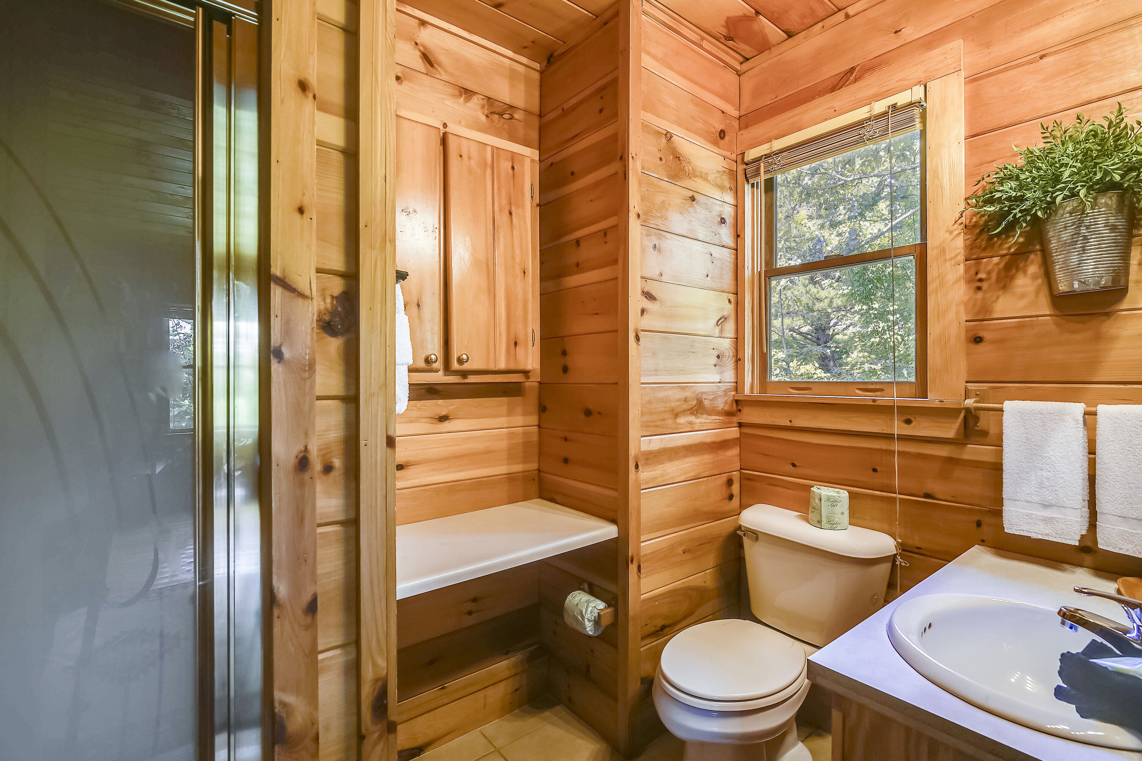 A wooden cabin bathroom with a toilet, sink, and window.