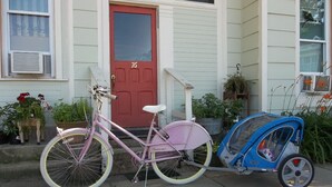 En rosa cykel med ett barnstol monterat, parkerad framför ett hus med en röd dörr och vit träpanel.