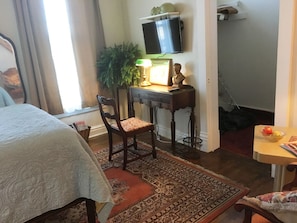 Relax in this inviting room with a comfortable bed, a desk for work, and a potted plant adding a touch of greenery.