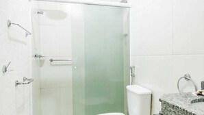 A modern bathroom with a glass shower enclosure, a white toilet, and a granite countertop sink. - Tokyo Hotel (Tres Lagoas)