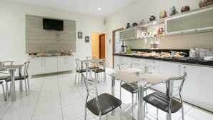 A modern kitchen with white cabinets, a flat-screen TV, and a dining area with glass tables and chairs. - Tokyo Hotel (Tres Lagoas)