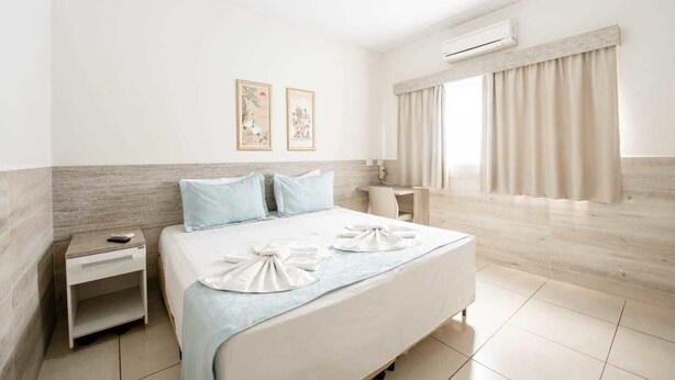 A hotel room with a bed, nightstand, and a window with curtains. - Tokyo Hotel (Tres Lagoas)