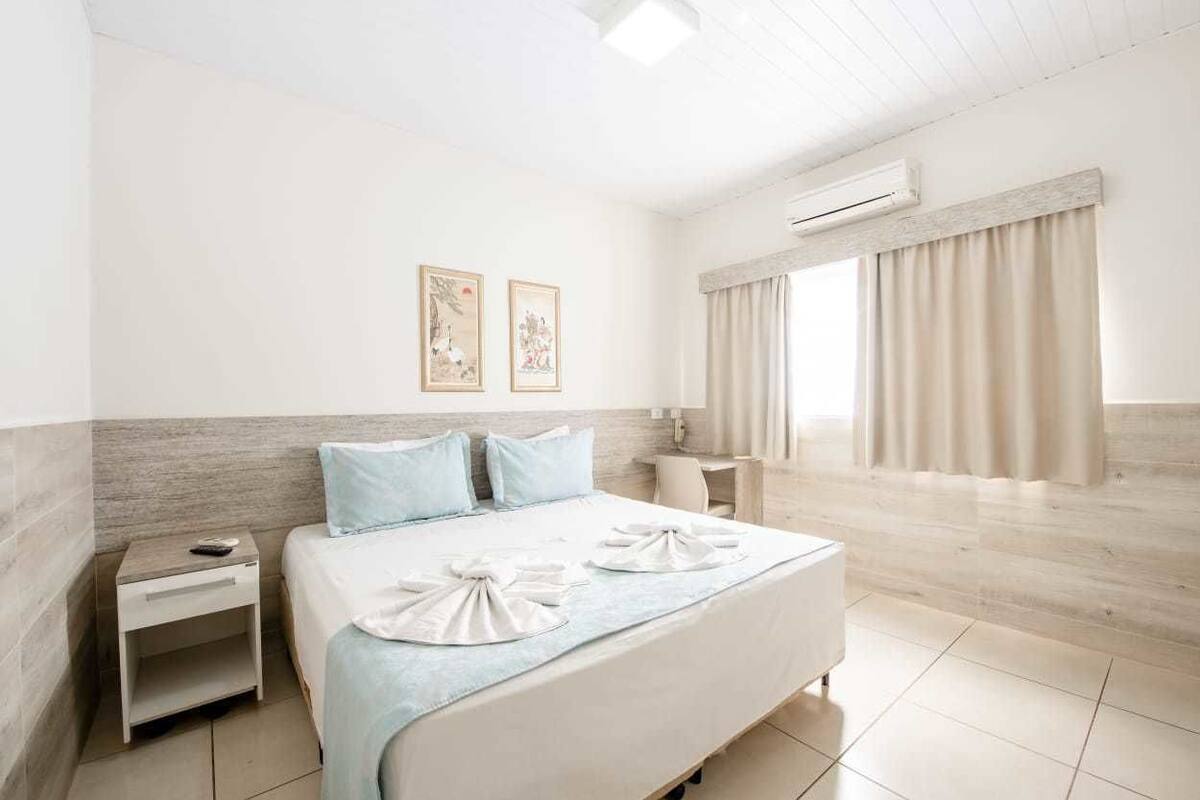 A hotel room with a bed, nightstand, and a window with curtains.