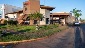 A modern hotel with a prominent red logo, a covered outdoor seating area, and a well-maintained lawn. - Tokyo Hotel (Tres Lagoas)