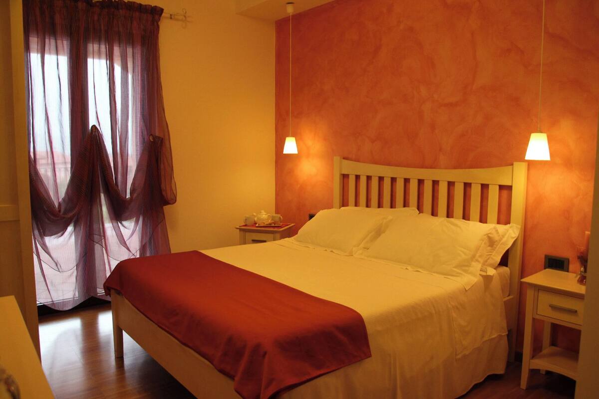 A hotel room with a bed, a nightstand, a lamp, and a window with curtains.