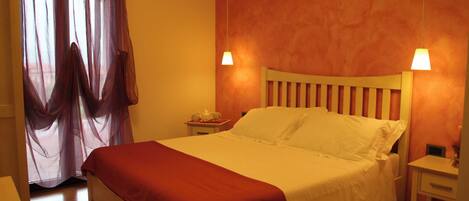 Ein Hotelzimmer mit Bett, Nachttisch, Lampe und einem Fenster mit Vorhängen.