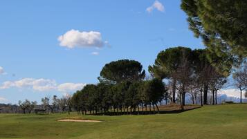 A golf course with a clear sky, trees, and a bench.