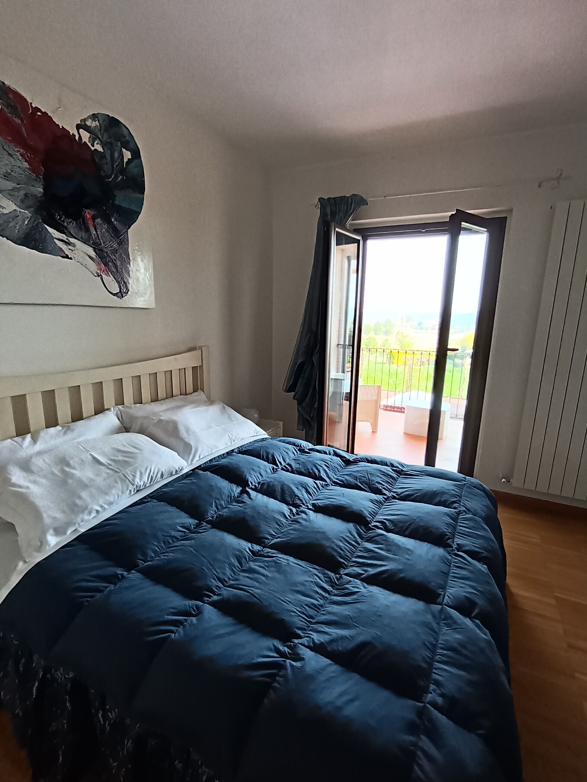 A bedroom with a bed, a painting, and a balcony.