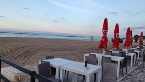 A beachside restaurant with outdoor seating, red umbrellas, and a view of the ocean. - Prati di Maja B&B (Miglianico)